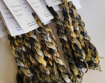 May include: Four skeins of twisted embroidery thread in a variegated colorway of moss green, black, and cream. Each skein is attached to a white paper tag labeled Night Stalker Calling with colorway Moss, dye lot 2, and 10 yards.