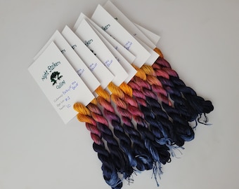 May include: Bundles of hand-dyed embroidery floss in a gradient of colors, from golden yellow to deep navy blue. Each bundle is paired with a white card labeled "Night Stalkers Calling" with "Betsy of the Beast" and other details.