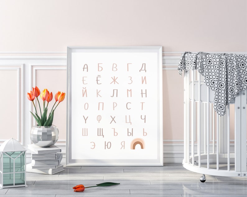 May include: A white framed print with the Cyrillic alphabet in pink and brown letters. The letters are arranged in a grid pattern. A rainbow with pink, orange, and yellow stripes is at the bottom of the print.