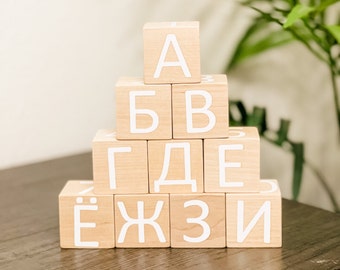 May include: A stack of wooden blocks with the letters A, Б, В, Г, Д, Е, Ё, Ж, З, И printed in white on each block.