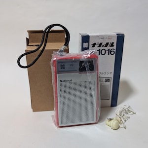 May include: A red and white National AM portable radio with a black wrist strap, encased in a clear plastic sleeve. The radio is accompanied by a brown cardboard box, a blue and white product box labelled 1016, and a white wired earphone.