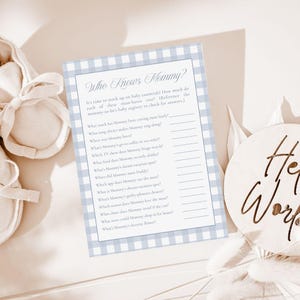 May include: A baby shower game card with a blue gingham border and the text "Who Knows Mommy?" in elegant script. The card includes fill-in-the-blank questions about the mother-to-be. A wooden sign that says "Her World" is also in the image.