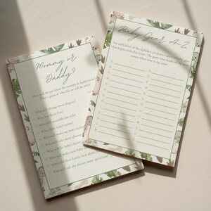 Puede incluir: Dos tarjetas de juego para baby shower. Una tarjeta se titula "&iquest;Mam&aacute; o Pap&aacute;?" con preguntas para completar. La otra tarjeta se titula "Baby Gear A-Z" con l&iacute;neas alfab&eacute;ticas. Ambas tarjetas tienen un fondo beige claro con un borde de hojas y animales verdes.