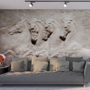 Może przedstawiać: Duży mural ścienny przedstawiający beżowy kamienny relief czterech koni z profilu. Mural znajduje się za długą, szarą, pikowaną sofą. W pomieszczeniu znajduje się st&oacute;ł jadalny z białymi krzesłami oraz złoty żyrandol wiszący powyżej.