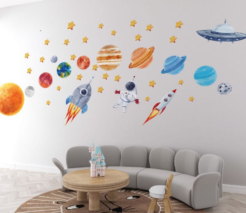 May include: A set of colorful space-themed wall decals featuring planets, stars, a rocket, an astronaut, and a UFO. The decals are perfect for a child's bedroom or playroom.