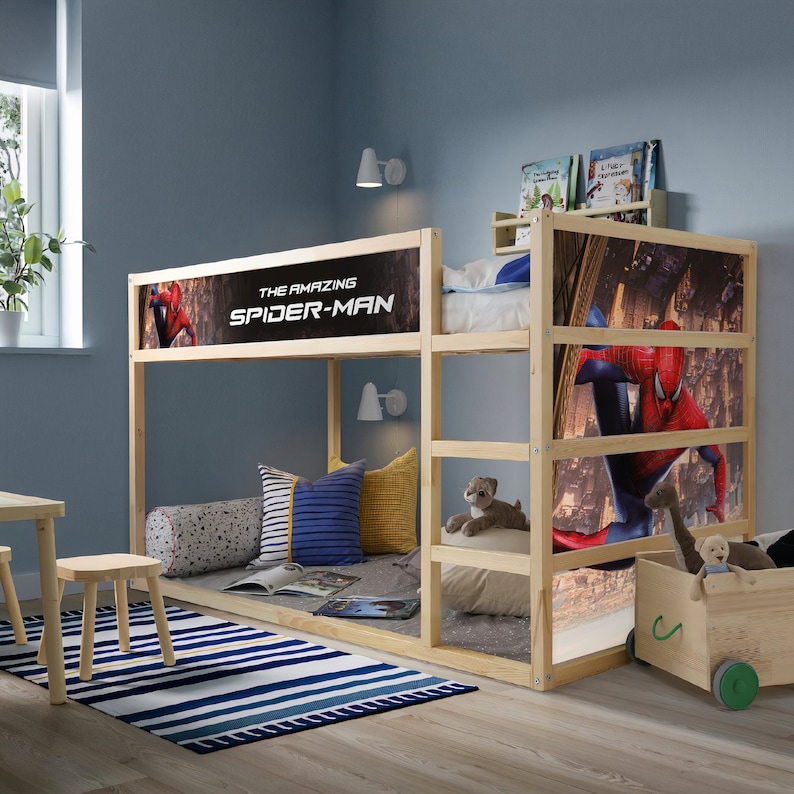 K&ouml;nnte beinhalten: Ein Holz-Hochbett mit einem Spiderman-Kopfteil. Das obere Bett hat ein rotes und blaues Spiderman-Motiv mit dem Text "The Amazing Spider-Man". Das untere Bett hat ein Spiderman-Motiv mit einem Stadt-Hintergrund.