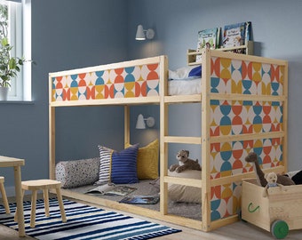 May include: A light-colored wooden loft bed featuring side panels with a repeating geometric pattern in orange, yellow, and blue. The structure includes a built-in ladder, a top bunk with bedding, and an open lower area with pillows and a small wooden toy cart.