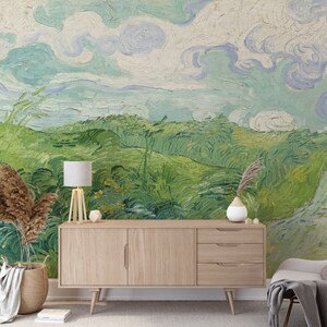 Puede incluir: Un mural de pared con una pintura de paisaje con nubes azules arremolinadas y colinas verdes vibrantes. Un aparador de madera clara con tres cajones y un armario se sit&uacute;a frente al mural, junto a una l&aacute;mpara, un jarr&oacute;n y una cesta tejida.