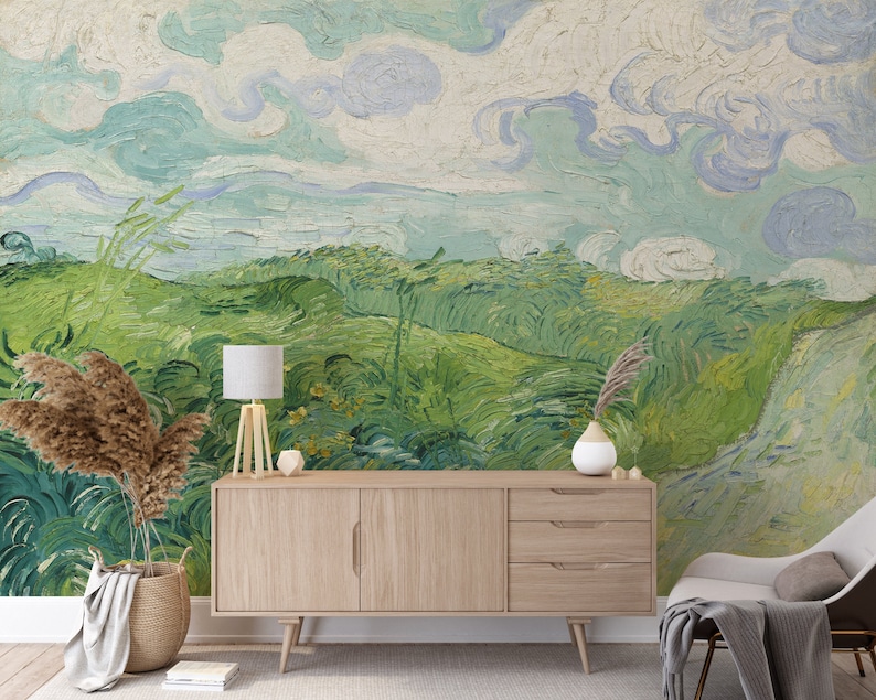 Puede incluir: Un mural de pared con una pintura de paisaje con nubes azules arremolinadas y colinas verdes vibrantes. Un aparador de madera clara con tres cajones y un armario se sit&uacute;a frente al mural, junto a una l&aacute;mpara, un jarr&oacute;n y una cesta tejida.