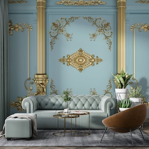 May include: A living room interior with a light blue wall featuring gold decorative moldings. A light blue sofa with a tufted design sits in front of the wall. A brown leather armchair sits to the right of the sofa. A gold metal coffee table with two tiers sits in front of the sofa. Two potted plants are on the right side of the image.