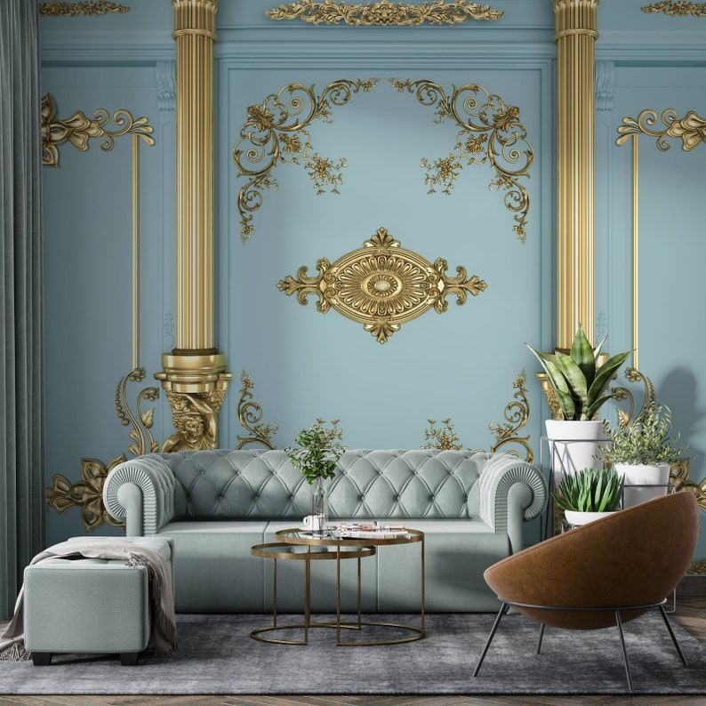 May include: A living room interior with a light blue wall featuring gold decorative moldings. A light blue sofa with a tufted design sits in front of the wall. A brown leather armchair sits to the right of the sofa. A gold metal coffee table with two tiers sits in front of the sofa. Two potted plants are on the right side of the image.