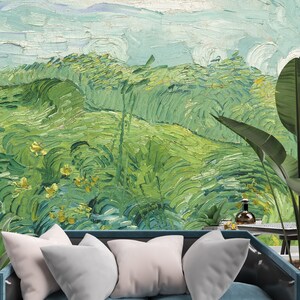 Puede incluir: Un sof&aacute; azul con cuatro cojines blancos frente a un mural de pared que muestra un paisaje verde con pinceladas gruesas, un cielo azul claro y flores amarillas, junto a una mesa peque&ntilde;a con una botella de vidrio.