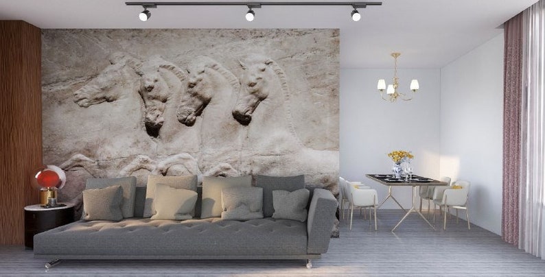 Może przedstawiać: Duży mural ścienny przedstawiający beżowy kamienny relief czterech koni z profilu. Mural znajduje się za długą, szarą, pikowaną sofą. W pomieszczeniu znajduje się st&oacute;ł jadalny z białymi krzesłami oraz złoty żyrandol wiszący powyżej.