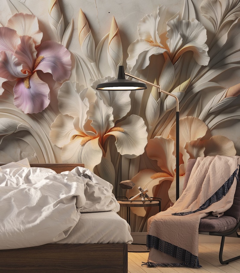 May include: A bedroom scene featuring a wall mural of large, sculpted, three-dimensional iris flowers in shades of soft pink, cream, and white. A black floor lamp with a gold arm stands next to a chair draped with a light pink and dark blue throw.