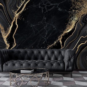 May include: A black tufted sofa with rolled arms sits before a wall featuring a black and gold marble-patterned mural. A round coffee table with a gold metal frame and a black glass top is positioned in front of the sofa on a geometric rug.