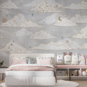 May include: A bedroom featuring a white bed with pink and grey polka dot pillows, a pink throw blanket, and a white storage bench holding five animal-shaped plush toys. The wall is covered in grey wallpaper with gold-outlined clouds, stars, and moons.