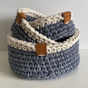 Puede incluir: Dos cestas de crochet en color azul y blanco. Las cestas tienen etiquetas de cuero con el texto "Atelier Pyssa" en ellas.