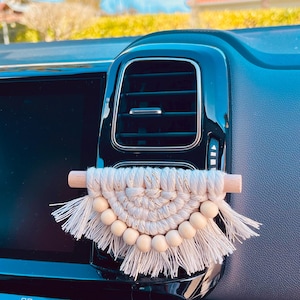 Peut inclure: Un diffuseur d'air de voiture en macramé blanc avec des perles en bois et des glands suspendus à l'aération d'une voiture.