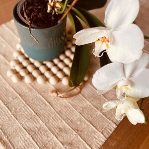May include: A white orchid plant in a blue pot with brown roots. The plant is on a white woven placemat with a wooden surface underneath.