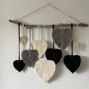 Peut inclure: Une suspension murale en macramé avec une branche de bois flotté et plusieurs motifs en forme de cœur en noir, blanc et gris.