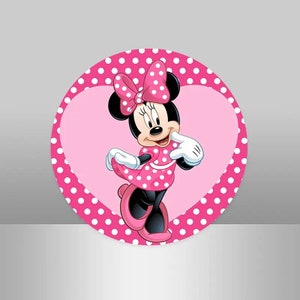 May include: A pink and white polka dot circle with a pink heart in the center. A cartoon image of Minnie Mouse is in the heart. Minnie Mouse is wearing a pink polka dot dress and a red bow.