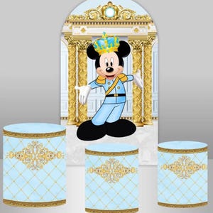 May include: A blue and gold themed party backdrop with a Mickey Mouse character wearing a crown and a blue and gold uniform. The backdrop features a white archway with gold columns and a blue and gold patterned floor. There are three blue and gold cylindrical cake stands in front of the backdrop.