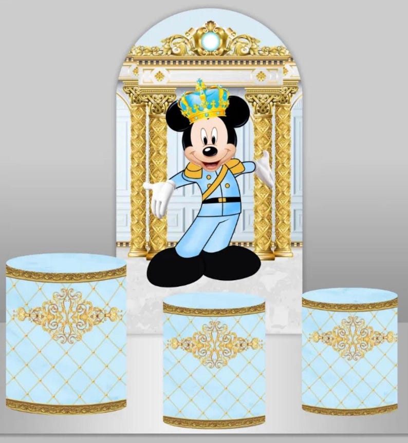 May include: A blue and gold themed party backdrop with a Mickey Mouse character wearing a crown and a blue and gold uniform. The backdrop features a white archway with gold columns and a blue and gold patterned floor. There are three blue and gold cylindrical cake stands in front of the backdrop.