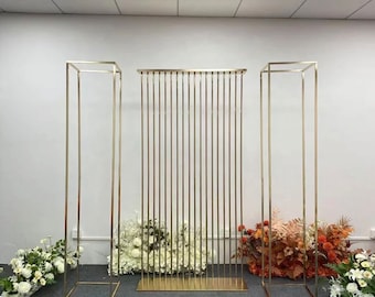 May include: Three gold metal archways, two are square and one is a tall rectangle with vertical bars. The arches are decorated with white and orange flowers.