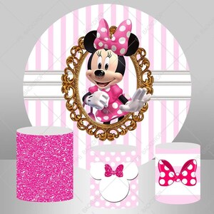 May include: Pink and white striped backdrop with a gold framed image of Minnie Mouse wearing a pink polka dot dress and a red bow. Three pink and white themed cake stands with glitter and polka dot designs.