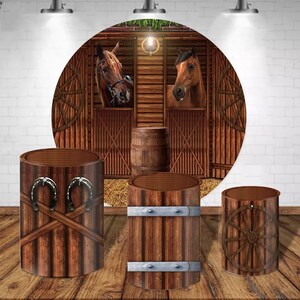 May include: Three wooden cylinder stands with different designs. The first stand has two horseshoes on the front. The second stand has two metal bands around the middle. The third stand has a wooden wagon wheel on the front. The stands are in front of a round backdrop with a wooden barn scene and two horses looking out of the stalls.