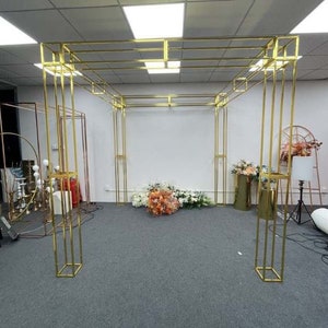 May include: A gold metal archway structure with a square base and multiple horizontal bars. The archway is standing on a gray carpet.