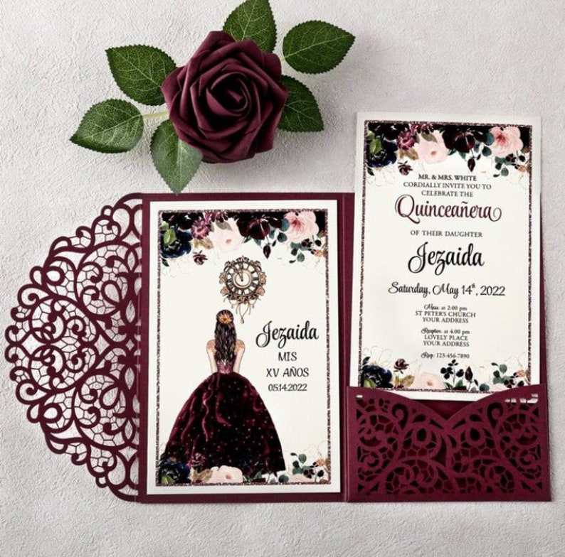 May include: Burgundy laser-cut invitation with a floral design and a pocket for a smaller card. The smaller card has a floral design and text that reads "MR. & MRS. WHITE CORDIALLY INVITE YOU TO CELEBRATE THE QUINCEA&Ntilde;ERA OF THEIR DAUGHTER Jezaida Saturday, May 14, 2022 At 2:00 PM ST. PETERS CHURCH YOUR ADDRESS Reception at 4:00 PM LOVELY PLACE YOUR ADDRESS RSVP 123-456-7890". The larger card has a floral design and a drawing of a girl in a burgundy dress with a clock behind her. The text on the larger card reads "Jezaida MIS XV A&Ntilde;OS 0514.2022".