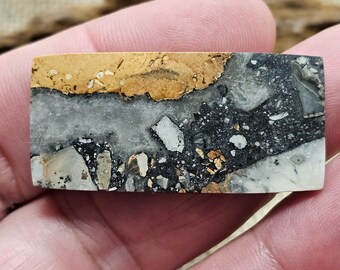 Puede incluir: Primer plano de una piedra pulida con un patrón único de negro, blanco y dorado. La piedra tiene una superficie lisa y pulida y una variedad de texturas.