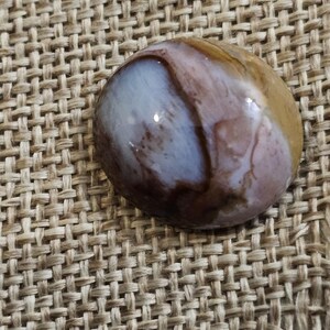 May include: A smooth, oval-shaped stone with brown, white, and pink swirling patterns. The stone is polished and has a glossy finish.