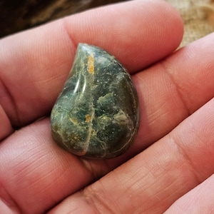 Könnte beinhalten: Ein tropfenförmiger grüner und goldener Edelstein mit einem marmorierten Muster.