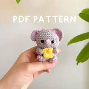 Puede incluir: Un juguete de amigurumi de elefante de crochet gris que sostiene un corazón de crochet amarillo. El elefante tiene orejas rosas y una nariz rosa.