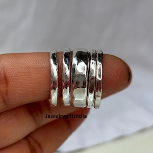 Könnte beinhalten: Ein Satz von fünf gehämmerten Silberringen. Die Ringe sind gestapelt und haben eine strukturierte Oberfläche. Die Ringe werden auf einem Finger präsentiert. Der Text "Jewelrygiftindia" ist unten sichtbar.