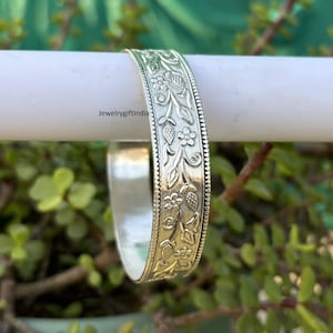 Może przedstawiać: Srebrna bransoletka z kwiatowym wzorem. Wzór zawiera skomplikowane detale liści i kwiatów.