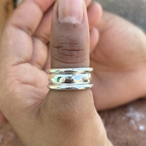 May include: A silver thumb ring with three bands. The bands are stacked on top of each other and have a hammered texture.