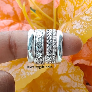 May include: A collection of silver rings with intricate floral and leaf patterns. The rings are displayed on a finger against a backdrop of yellow and orange flowers. The text "JewelrygiftIndia" is visible.