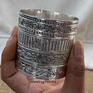 Op de afbeelding: Zilveren armband met ingewikkelde bloem- en geometrische ontwerpen. De armband is gemaakt van gepolijst zilver en heeft een brede, platte band.