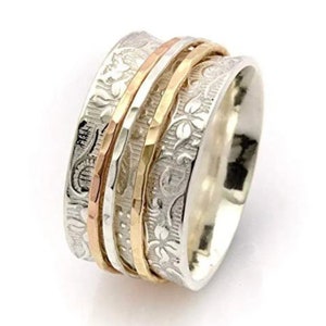 May include: A silver spinning ring with three bands of gold. The ring is decorated with a floral pattern.