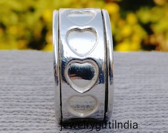 Può includere: Un anello d'argento con una fascia girevole che presenta quattro disegni a forma di cuore. L'anello è su una superficie grigia testurizzata.
