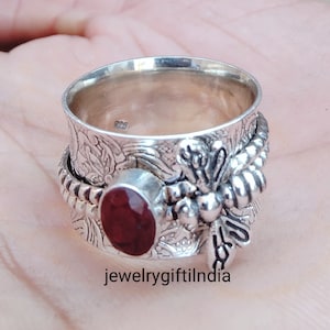 May include: A silver spinning ring featuring a red gemstone and a dragonfly design. The ring is engraved with floral patterns.