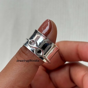 May include: A silver-colored ring with an infinity symbol design. The ring is wide and has a spinning band. The text "Jewelrygiftindia" is visible on the ring. The ring is on a finger.