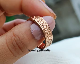 May include: A gold-coloured ring with a repeating circular pattern is shown close-up. The ring is held between two fingers. The text "JewelrygiftIndia" is visible at the bottom of the image.