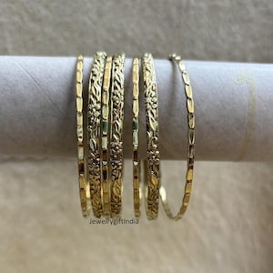 May include: A set of seven gold-toned bangles with intricate floral designs. The bangles are stacked on top of each other and are arranged in a circular pattern.