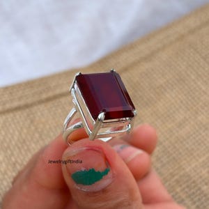 Könnte beinhalten: Ein Silberring mit einem großen, rechteckigen, tiefroten Edelstein. Der Ring hat ein geteiltes Schaftdesign und eine Fassung, die den Stein sicher hält. Das Bild enthält den Text "jewelrygiftindia".