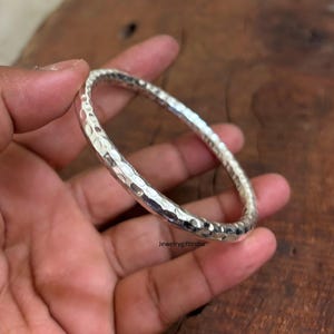 May include: A silver hammered bangle bracelet. The bracelet is round and has a smooth, polished finish.