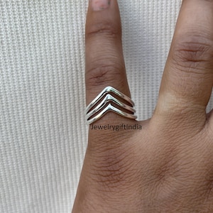 Peut inclure: Bague en argent avec trois bandes en chevron superposées. La bague est portée au doigt.